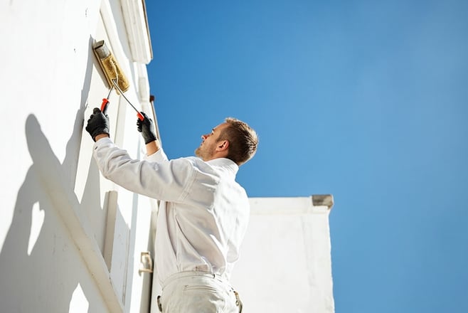 professional painter painting exterior wall of house with paint roller, blue sky